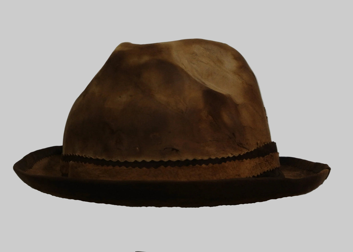 Brown amadou fedora hat on a white stand against a plain background
