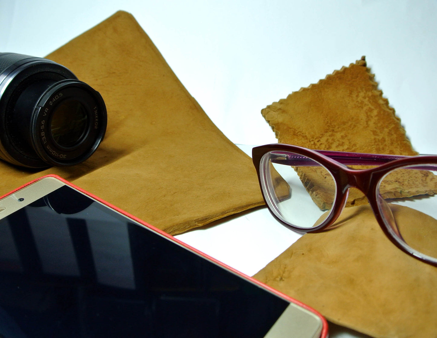 Camera lens, phone, and glasses on a brown leather surface with a white background