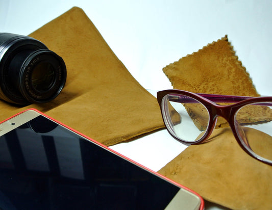 Camera lens, phone, and glasses on a brown leather surface with a white background