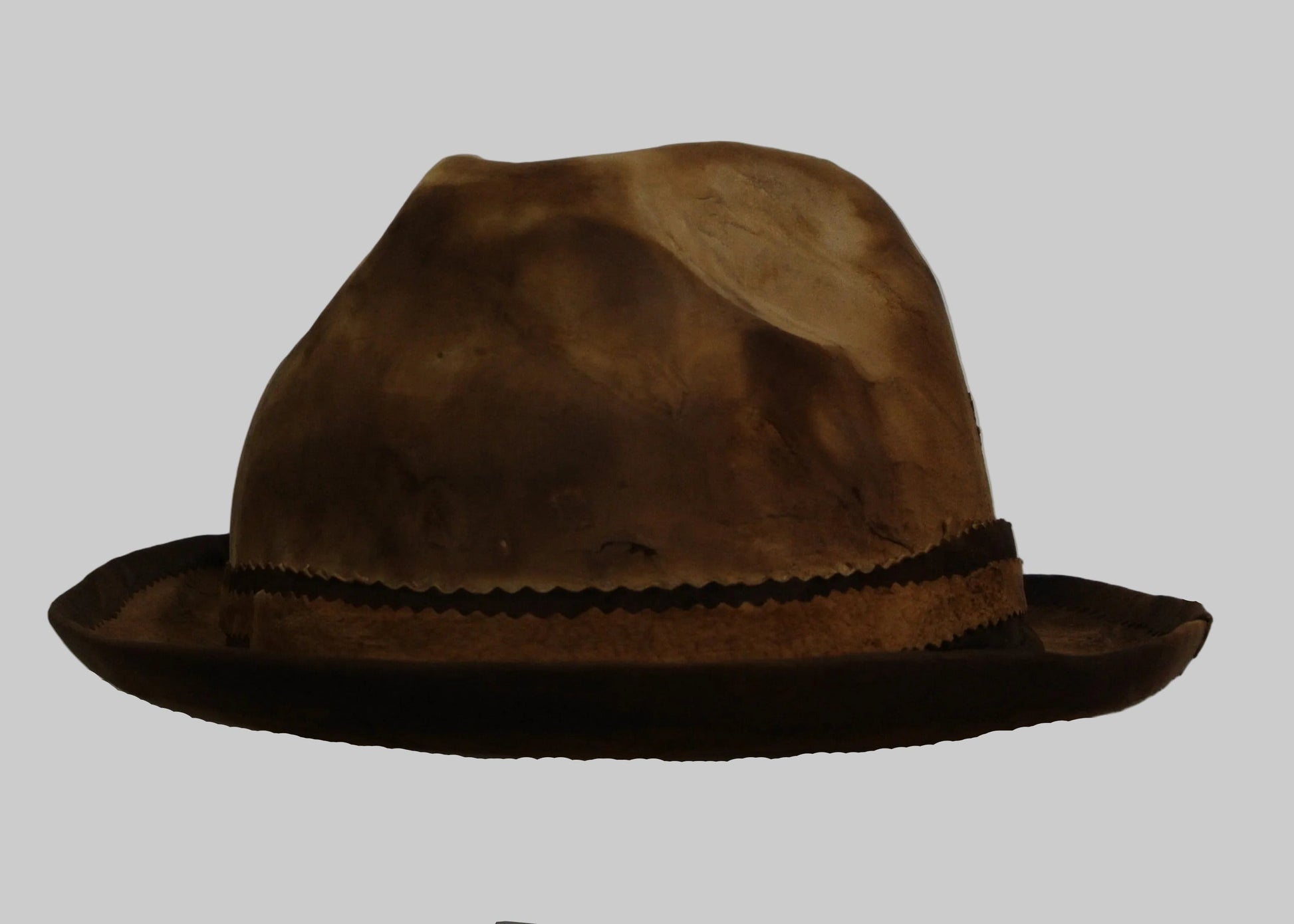 Brown amadou fedora hat on a white stand against a plain background
