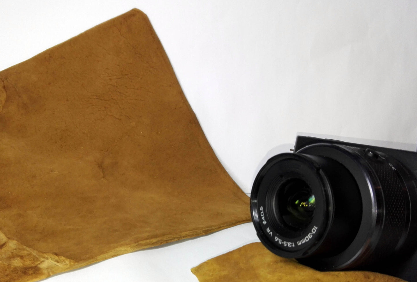 Camera lens on a white surface with a brown amadou lens cleaner beside